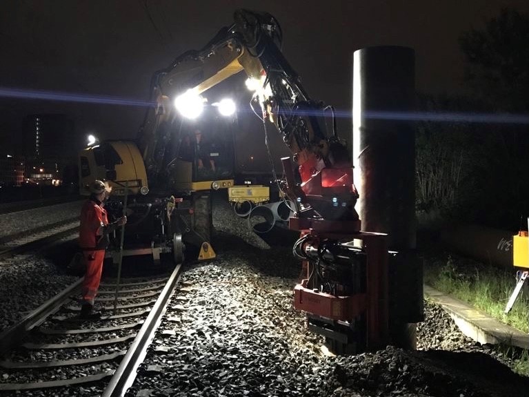 Ein Bagger und Bauarbeiter auf den Gleisen bei Nacht