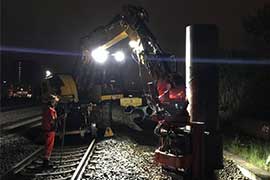 Ein Bagger und Bauarbeiter auf den Gleisen bei Nacht